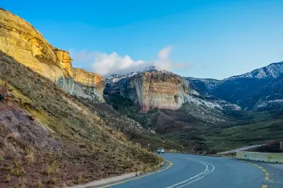 Mountain road passing beneath sandstone cliffs and snow-dusted peaks in Golden Gate Highlands National Park, South Africa.