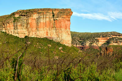 Brandwag Buttress, a massive sandstone cliff formation in Golden Gate Highlands National Park, South Africa, with layered orange and cream rock faces rising above green vegetation and surrounding mountain valleys.