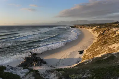 Wide coastal view of Grotto Beach with dunes, surf lines, and Walker Bay coastline near Hermanus in the Western Cape, South Africa.
