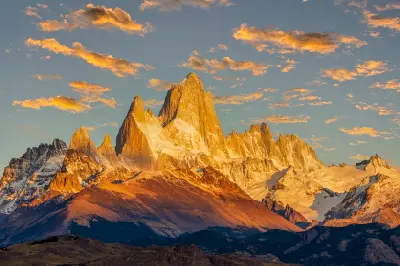 Mount Fitz Roy glowing in warm sunrise light with surrounding peaks and clouds in Patagonia, Argentina.