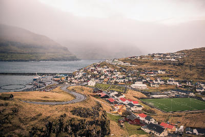 Overhead view of Eiði with winding road, harbor and colorful houses on Streymoy, Faroe Islands.
