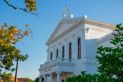 Historic Ou Hoofgebou academic building at Stellenbosch University in Stellenbosch, South Africa, framed by trees in evening light.