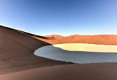 Red sand dunes enclosing a pale clay pan in the Hiddenvlei area of Sossusvlei, Namibia.