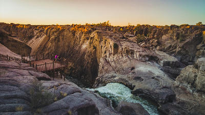 Viewpoint above the granite gorge at Augrabies Falls, with a viewing deck overlooking the Orange River canyon at sunset.
