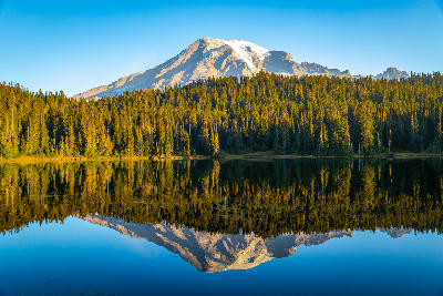 Mount Rainier reflected in Reflection Lakes with calm water, forest shoreline, and snow-covered peak in Mount Rainier National Park.