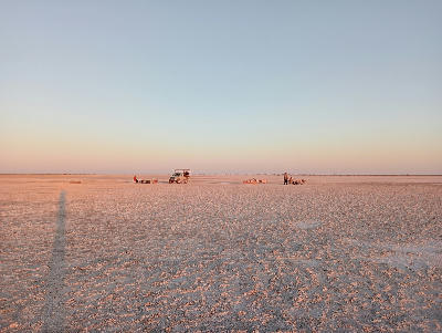 Sunset over the vast white salt flats of Makgadikgadi Pans in Botswana with a safari vehicle on the horizon.