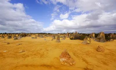 Hundreds of limestone pinnacles rise from yellow sand beneath a dramatic cloud-filled sky.