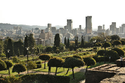 View across the formal gardens of the Union Buildings toward Pretoria's skyline, with government grounds and city towers framed by landscaped terraces.