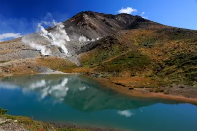 Sugatami Pond reflecting Mount Asahidake with volcanic steam vents rising from the slopes, Daisetsuzan National Park, Hokkaido, Japan.