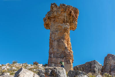 Hiker standing beneath the towering Maltese Cross rock formation in the Cederberg Mountains, illustrating the scale of this iconic sandstone landmark.