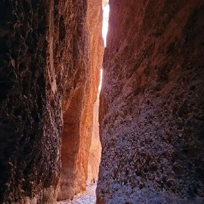 Visitors are dwarfed by the towering narrow walls of Echidna Chasm as sunlight illuminates the orange rock passage.