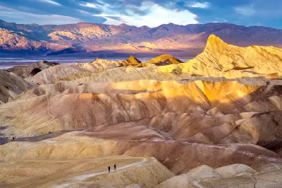 Hikers walking along Zabriskie Point ridges at sunrise in Death Valley National Park California with golden badlands landscape