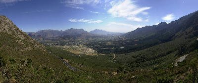Wide panorama from Franschhoek Pass showing the Franschhoek Valley, winding mountain roads, and rugged Cape Winelands mountain ranges in the Western Cape, South Africa.