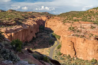 Burr Trail Road winds between towering red sandstone cliffs through Long Canyon beneath a cloud-filled sky.