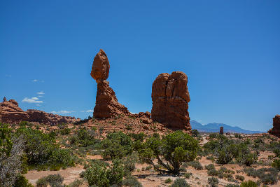 Balanced Rock perched on narrow base with nearby rock formations and desert vegetation under clear sky in Arches National Park Utah