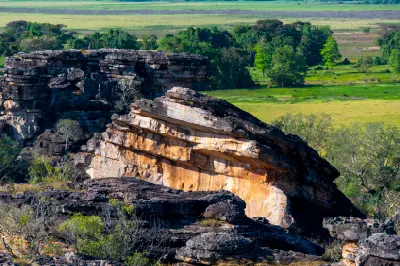 Layered orange and dark sandstone outcrops overlooking green floodplains at Ubirr in Kakadu National Park, Northern Territory, Australia.