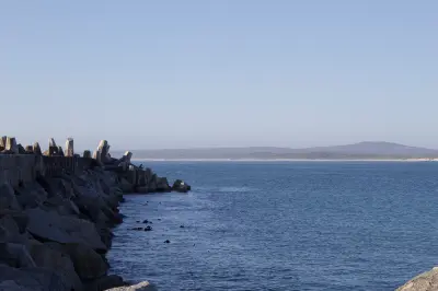 Concrete harbour breakwater and granite boulders at Yzerfontein Harbour, with calm Atlantic waters and distant coastal dunes visible across the bay.