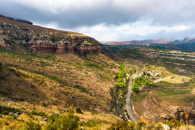 View across a valley in Golden Gate Highlands National Park with sandstone cliffs, rolling grasslands, a winding road and highland scenery beneath low cloud.