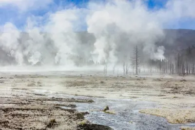 Icy meadow with a winding stream and rising steam from geothermal vents near the Lower Geyser Basin in Yellowstone National Park, Wyoming.