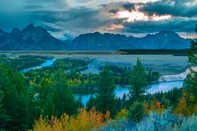 Snake River curving through green and autumn forest with the Teton Range under moody clouds, viewed from Snake River Overlook, Grand Teton National Park, Wyoming.