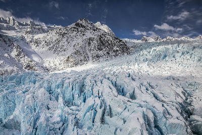 Jagged blue ice formations of Franz Josef Glacier beneath snow-covered peaks in Westland Tai Poutini National Park, New Zealand.