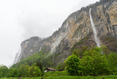 Staubbach Falls flowing down a high cliff in misty conditions above green valley floor in Lauterbrunnen Switzerland