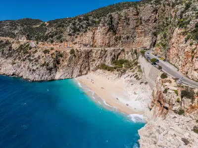 Aerial view of Kaputaş Beach, with turquoise water, a sandy cove, steep limestone cliffs and the coastal road winding above the beach.