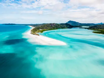 Aerial view along Whitehaven Beach with white silica sand, turquoise water and forested hills on Whitsunday Island, Queensland.