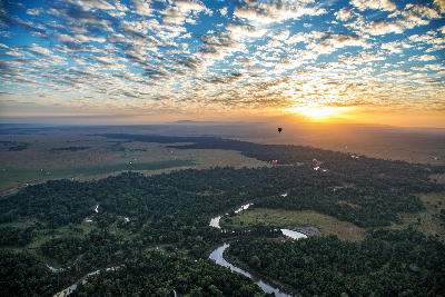 Hot air balloons flying above the Mara River and northern Serengeti landscape at sunrise in Tanzania.