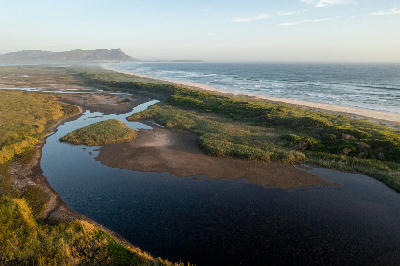 Aerial view of the Kleinmond Estuary flowing through coastal wetlands and dunes beside the ocean along the Overberg coastline in South Africa.