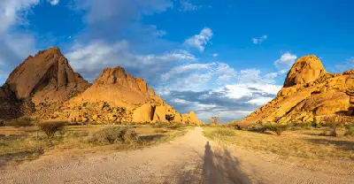 Desert road leading between granite formations at Spitzkoppe in Namibia under blue sky and golden evening light.