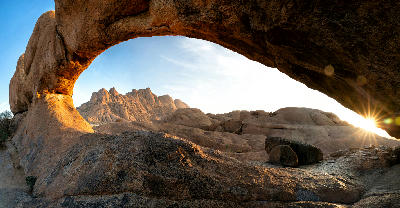 Granite arch at Spitzkoppe in Namibia framing desert mountains during sunrise with warm golden light.