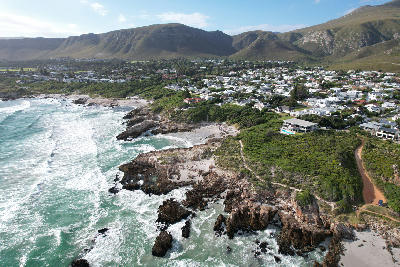 Aerial view of the rocky Hermanus coastline with mountain backdrops and coastal neighbourhoods along Walker Bay, South Africa