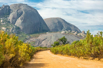 Dirt road through fynbos vegetation leading toward the towering rounded granite domes of Paarl Rock in Paarl Mountain Nature Reserve, South Africa.