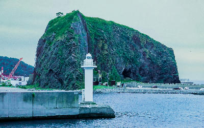 Oronko Rock rising above Utoro Port with a small lighthouse and harbour structures in the foreground, Shiretoko Peninsula, Hokkaido, Japan.