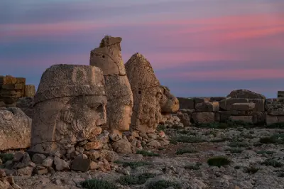 Ancient colossal stone heads on Mount Nemrut beneath a pink sunrise sky.