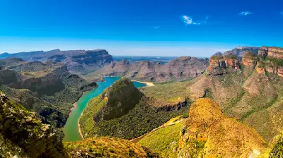 Panoramic view of Blyde River Canyon and the Three Rondavels in Mpumalanga, South Africa, with the winding Blyde River, steep cliffs, rugged mountains and expansive canyon scenery under a clear blue sky.