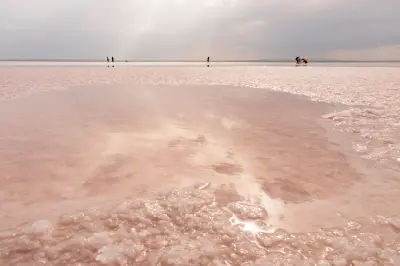 Pink shallow water and white salt crystals at Lake Tuz, with visitors walking across the vast salt flats in the distance, Turkey.