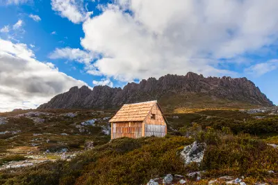 Wooden mountain shelter beneath the rugged Cradle Mountain ridgeline in Tasmania, Australia.
