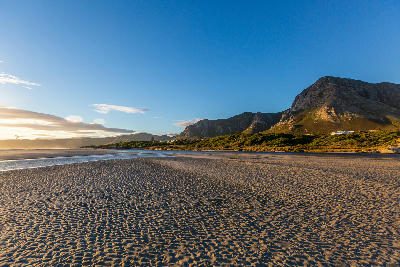 Golden evening light across the rippled sand flats and shoreline of Grotto Beach beneath the Hermanus mountains in South Africa