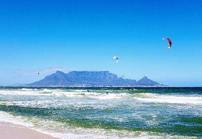 Kitesurfers riding waves at Bloubergstrand beach with Table Mountain and Lion’s Head across Table Bay, Cape Town, South Africa.