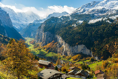 View from Wengen over Lauterbrunnen Valley with Staubbach Falls, autumn forest, and snow-covered peaks in the Bernese Oberland, Switzerland.