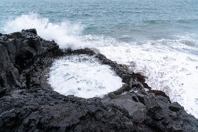Sea waves crashing into the circular Brimketill lava pool surrounded by black volcanic rock on the Reykjanes Peninsula, Iceland.