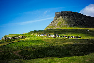 Gásadalur village surrounded by green hills and a flat-topped mountain on Vágar Island, Faroe Islands.