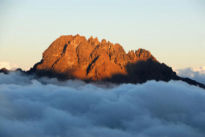 Golden evening light illuminating Mawenzi Peak (5,149 m) above clouds on Mount Kilimanjaro, Tanzania, viewed from approximately 4,700 metres above sea level.