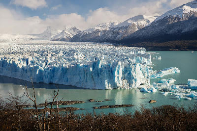 Perito Moreno Glacier ice wall extending into turquoise lake with mountains and forest foreground in Patagonia, Argentina.