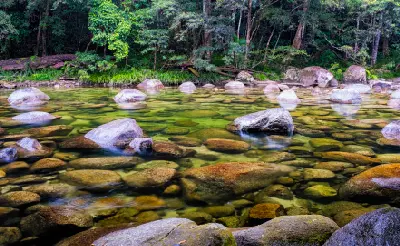 A tranquil, wide shot of a shallow river bed filled with multi-coloured rocks and large granite boulders bordered by trees.