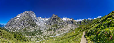 Mountain trail on grassy slopes leading toward granite peaks in the Chamonix Valley, France.