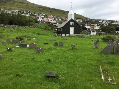 Black wooden Sørvágur Church with white tower and surrounding graveyard in Sørvágur on Vágar Island, Faroe Islands.