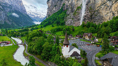 Lauterbrunnen village church with Staubbach Falls cascading down steep cliff walls in the Bernese Oberland, Switzerland.